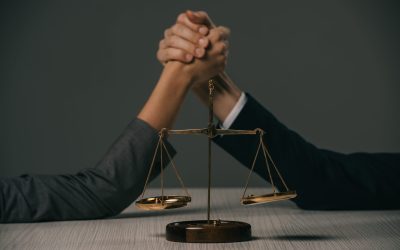 cropped view of businesspeople arm wretsling on wooden table with scales of justice on grey